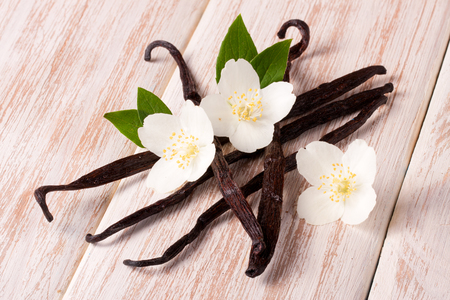 Vanilla sticks with flower and leaf on a white wooden background. Фото со стока