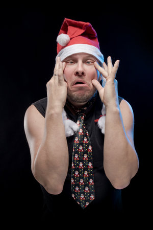 Emotional comic actor man in cap with braids gesticulates on a black background, in anticipation of Christmas and New Year