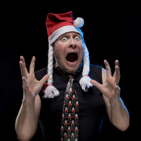 Emotional comic actor man in cap with braids gesticulates on a black background, in anticipation of Christmas and New Year