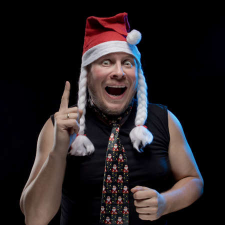 Emotional comic actor man in cap with braids gesticulates on a black background, in anticipation of Christmas and New Year