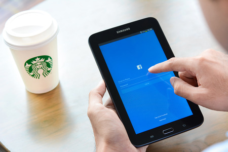 logo samsung: A man opening Fackbook application log in page on Samsung Galaxy Tab3 tablet with Starbucks coffee cup on the table.