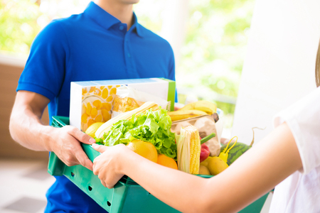 Delivery man delivering food to a woman at home - online grocery shopping service concept