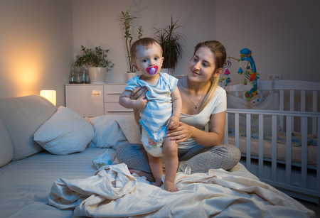 夜のベッドの上の彼女の赤ちゃん息子におむつ愛情深い母親 の写真素材 画像素材 Image
