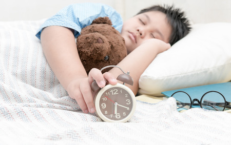 hand boy reaching to turn off alarm clock on the bed in the morning.