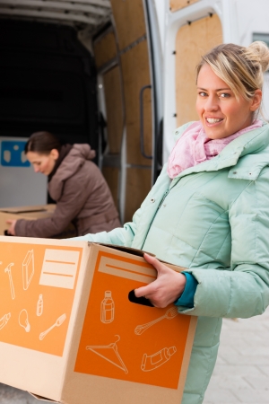 Two young women loading into a moving truck, they carry moving boxes