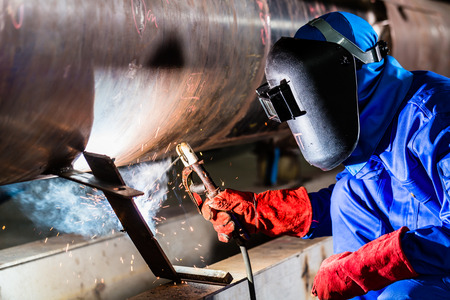 Welder in factory welding metal pipes Фото со стока