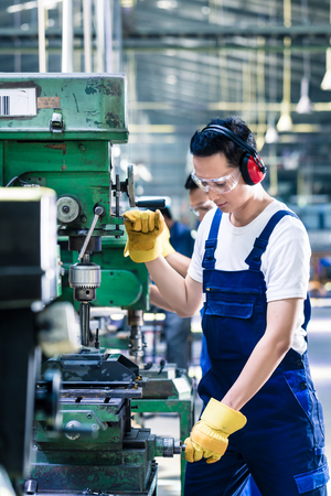 Asian worker in production plant drilling at machine on the factory floor