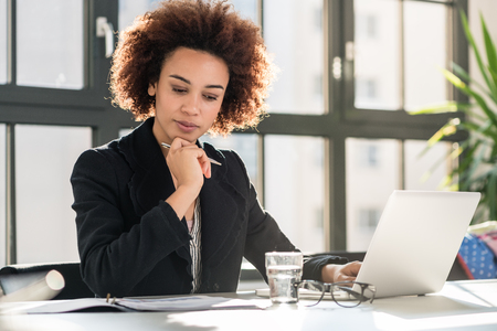 Portrait of African American female expert analyzing printed business report while sitting at desk in the office