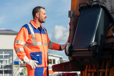 Garbage collection worker putting bin into waste truck for removal