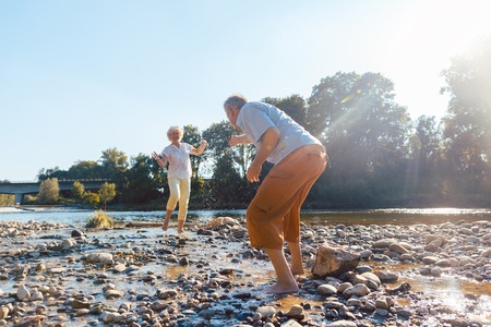Full length of a funny senior couple playing with water at the river while enjoying their happy relationship in a sunny day of summer Stockfoto