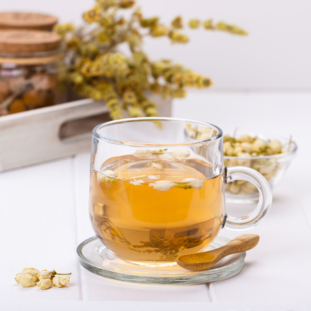Glass cup of organic asian jasmine tea with flowers on white wooden background