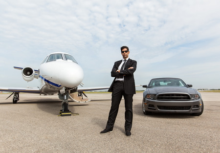 Full length of confident businessman standing by car and private jet at airport terminal