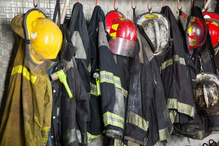 ropa de trabajo: Trajes de bombero y cascos que cuelgan en la estación de bomberos Foto de archivo