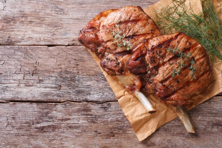 grilled pork: hai miếng thịt lợn nướng với các loại thảo mộc trên một tờ giấy vào một bảng cũ đầu xem ngang close-up