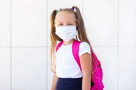 Schoolgirl stands with a backpack in a protective medical mask