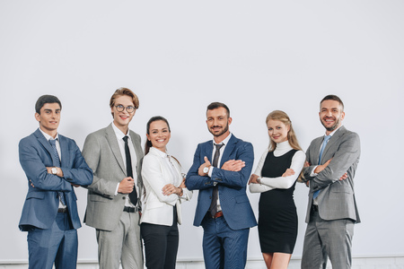 Smiling businesspeople with crossed arms posing near board after training in hub