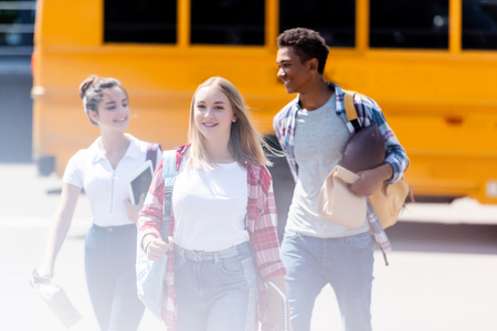 Group of happy teen students walking in front of school bus