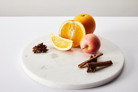 Close up view of fresh apple, oranges and spices ingredients for mulled wine on white surface