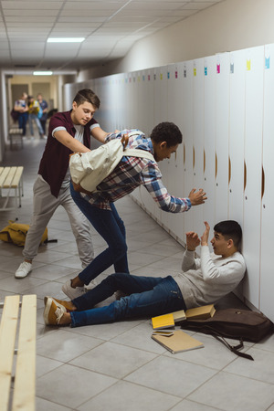 Asian and African American schoolboys being bullied in school corridor by their classmate Foto de archivo - 110950229