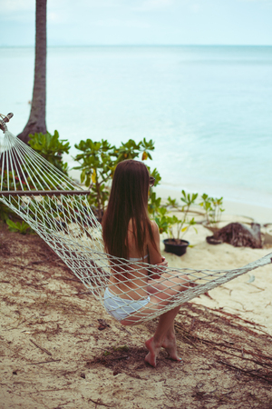 Back view of woman in bikini resting in hammock with ocean on background
