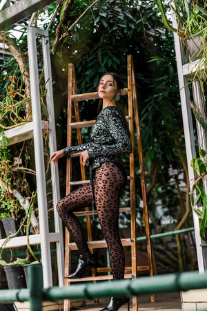 Woman in black pantyhose standing near wooden ladder in orangery