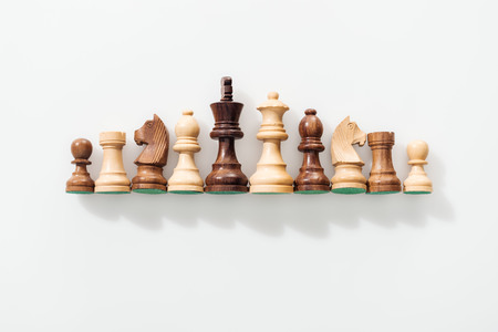 Top view of row made of brown and beige wooden chess figures on white background