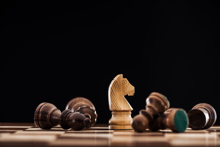 Selective focus of chessboard with scattered wooden figures and knight isolated on black