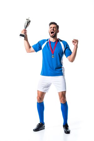 Excited soccer player with trophy cup and medal isolated on white