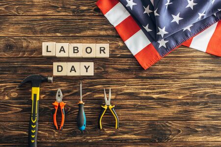 Top view of american flag near instruments and cubes with labor day lettering on wooden surface