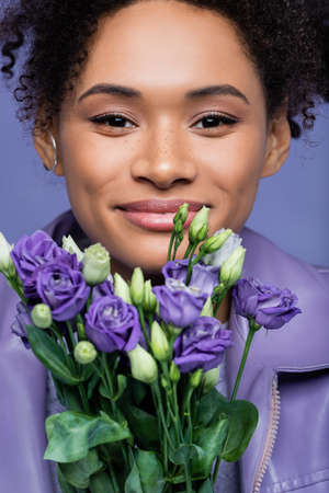 Smiling Young African American Woman Near Violet Flowers Isolated On Purple