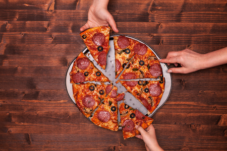 Hands taking pizza slices off the baking pan top view copy space