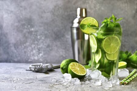 Cytrusowy koktajl mojito z limonką i miętą w wysokiej szklance na jasnoszarym tle łupkowym, kamiennym lub betonowym.
