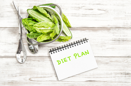 green salad leaves and vegetables with diet plan journal on white