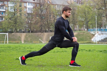 若い魅力的な男性アスリート スタジアムでウォーミング アップ ストレッチ運動 スクワット Lungesin の黒ジャージを作る の写真素材 画像素材 Image
