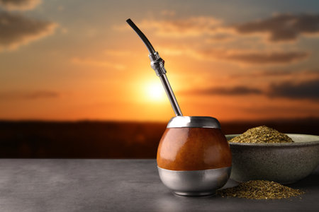 Calabash with mate tea and bombilla on light gray table outdoors at sunset. space for text