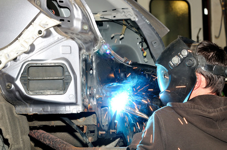 Body shop worker welding car panel.