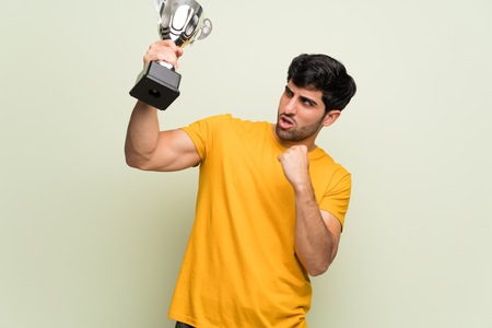 Young man over pink wall holding a trophy