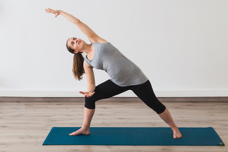 Young pregnant woman doing extended side angle yoga posture Stock Photo