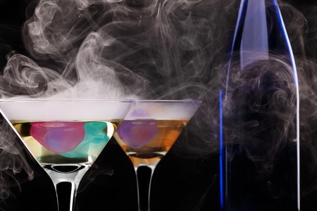 Wine glasses with colored ice cubes and dark blue bottle in floated ice vapor on black background. selective focus Stock Photo