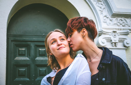 Girls couple standing kissing in a dark green door on the street