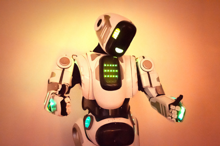 Robot close up the robot stands with his hands up and his fingers folded into the form of a class and tilting his head on an orange background concept of 4 industrial revolution