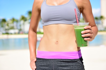 Fitness femme buvant un smoothie de légume vert après avoir exécuté l'exercice. Gros plan de smoothie et d'estomac. Concept de mode de vie sain avec modèle féminin en forme sur la plage.
