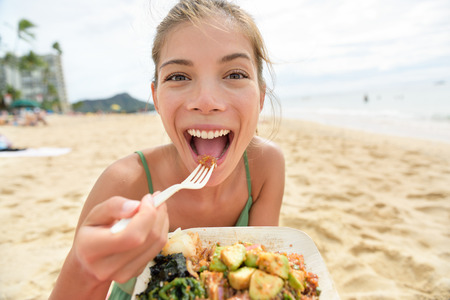 Lustige Frau, die gesunde Mahlzeit des Salats auf Strand in Hawaii isst. Foto auf Lager