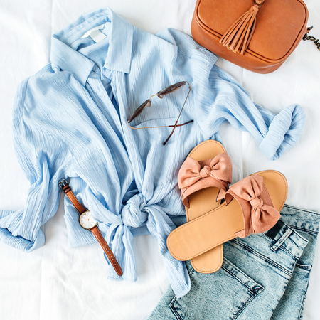 Feminine summer fashion composition with blouse, slippers, purse, sunglasses, watch, jean shorts on white background. flat lay, top view minimalist clothes collage. female fashion blog, social media, website concept.