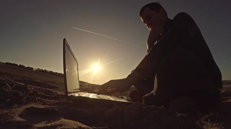 太陽の下でビーチ フリーランスのシルエットの上に座って後ろに男性ビジネスマン フリーランサー作業ノート パソコン の写真素材 画像素材 Image