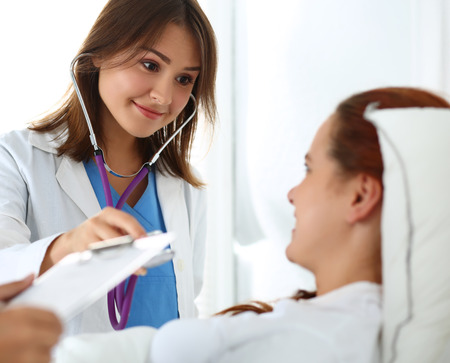 Female medicine doctor communicating examining and listening with stethoscope patient during ward ro Stock Photo Female medicine doctor communicating, examining and listening with stethoscope patient during ward round while nurse filling in patient medical history list. Medical care or insurance concept Stock Photo - 42963537