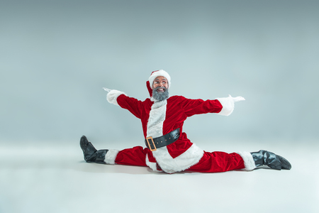 Funny serious guy with christmas hat dancing at studio. new year holiday. christmas, x-mas, winter, gifts concept. man wearing santa claus costume on gray. copy space. winter sales. Stock Photo