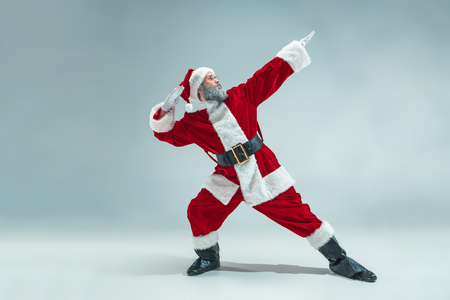 Funny serious guy with christmas hat dancing at studio. new year holiday. christmas, x-mas, winter, gifts concept. man wearing santa claus costume on gray. copy space. winter sales.