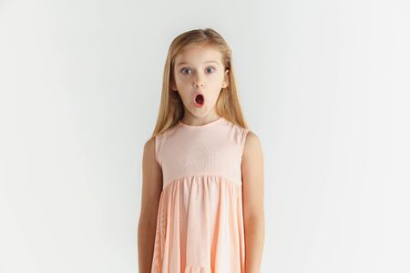 Stylish little smiling girl posing in dress isolated on white studio background. Caucasian blonde female model. Human emotions, facial expression, childhood. Wondered, astonished, shocked. Stock Photo