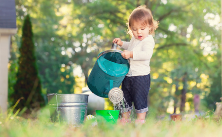 Happy toddler girl playing with watering cans outside Фото со стока